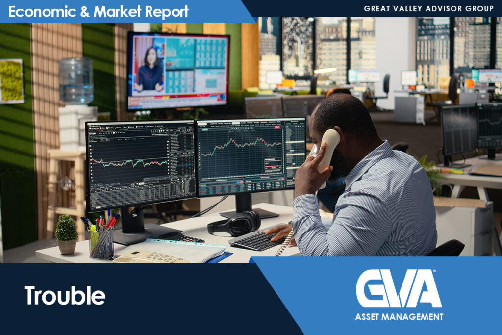Trader at a desk with three monitors showing stock charts, speaking on a landline phone.