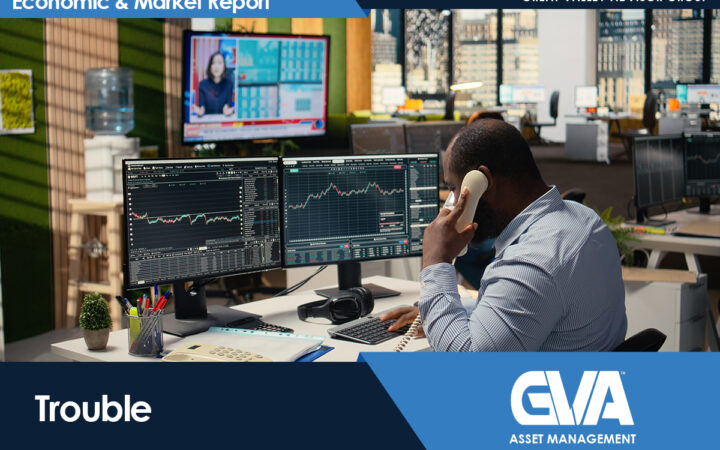 Trader at a desk with three monitors showing stock charts, speaking on a landline phone.